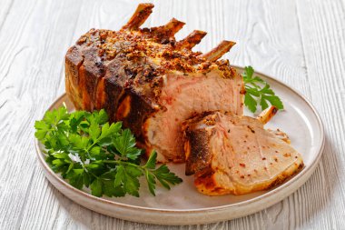 Standing Pork Rib Roast cut  on chops with  tomato sauce, mustard and parsley on white wood table, landscape view clipart