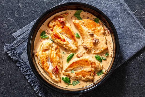 Chicken Breast Cutlets With Sun-Dried Tomato Cream Sauce in black baking dish on concrete table, flat lay, close-up