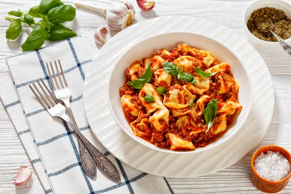 Stock image tortellini in ground beef tomato sauce in white bowl on white wood table with forks