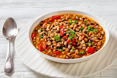 Vegan Hoppin John, savory and spicy black-eyed pea stew in black bowl on dark wood table, southern America recipe, horizontal view from above clipart