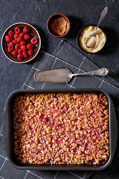 Raspberry Crumble Sheet Pan Pie on concrete table with cake shovel, fresh raspberries, brown sugar and cinnamon, vertical view from above, flat lay