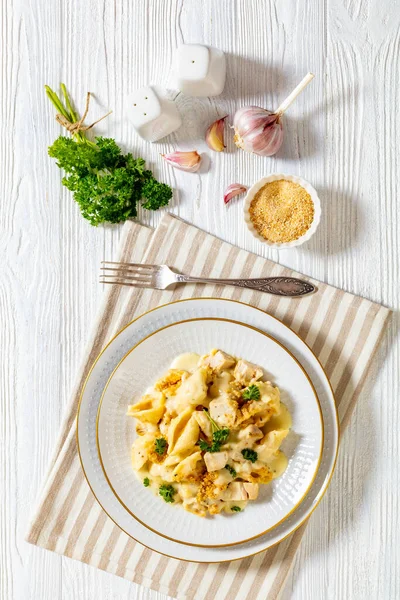 cheesy and creamy chicken and shells pasta bake in white bowl on white table, vertical view from above