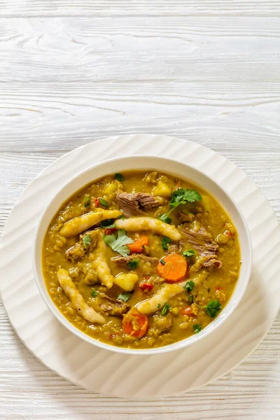gungo peas, pigeon peas soup with dumplings , vegetables and beef in white bowl on white wood table, jamaican cuisine, vertical view, free space