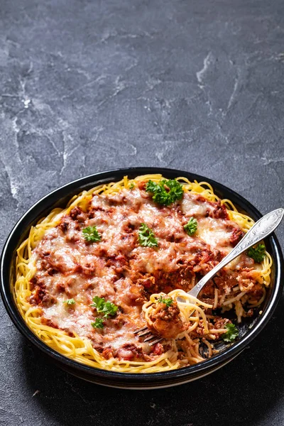 baked spaghetti layered with ground beef and marinara sauce, ricotta cheese and topped with mozzarella cheese in baking dish on concrete table, vertical view, free space