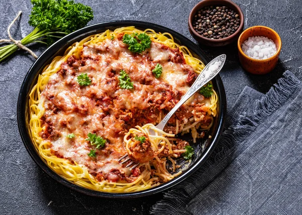 baked spaghetti layered with ground beef and marinara sauce, ricotta cheese and topped with mozzarella cheese in baking dish with fork on concrete table