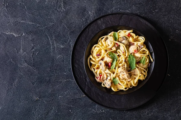 Chicken-Pepper Mushroom Alfredo linguine sprinkled with fresh sage leaves in black bowl on concrete table, horizontal view from above, flat lay, free space