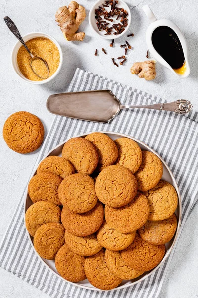 sweet and spicy soft ginger cookies on white plate on white table with ingredients on background, vertical view from above