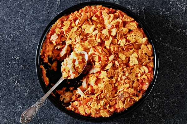 stock image tortilla chips chicken cheese casserole in baking dish with spoon on concrete table, horizontal view from above, flat lay, close-up