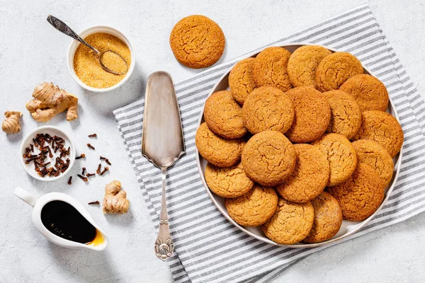 sweet and spicy soft ginger cookies on white plate on white concrete table with ingredients on background, horizontal view from above, flat lay