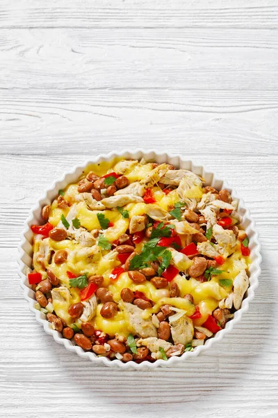 close-up of shredded chicken breast, pinto beans, tomato and mozzarella in white round baking dish on white wood table, vertical view, free space