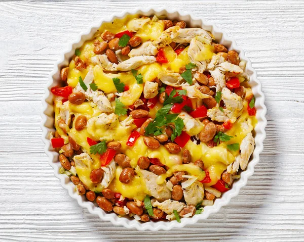 shredded chicken breast, pinto beans, tomato and mozzarella in white round baking dish on white wood table, horizontal view from above, flat lay, close-up