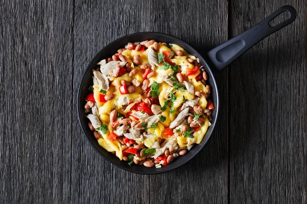 one pan dinner of shredded chicken breast, pinto beans, tomato and mozzarella on dark wood table, horizontal view from above, flat lay, free space