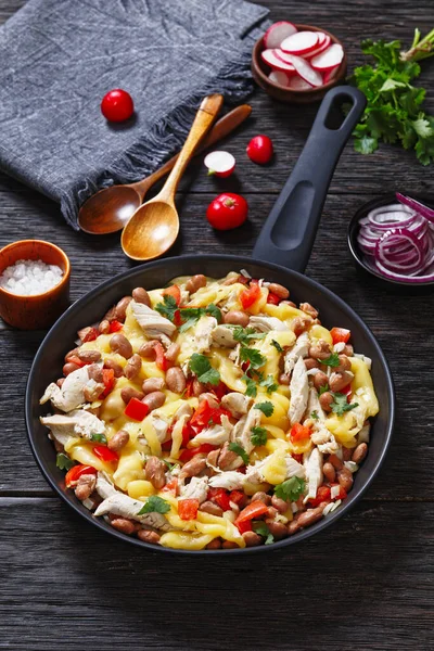 one pan dinner of shredded chicken breast, pinto beans, tomato and mozzarella on dark wood table, vertical view from above