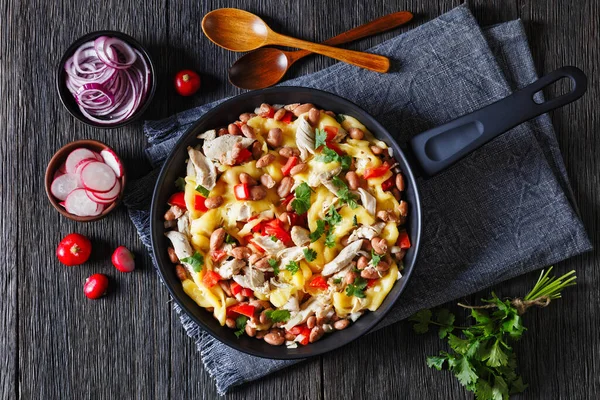 one pan dinner of shredded chicken breast, pinto beans, tomato and mozzarella on dark wood table with wooden spoons,  red radish, horizontal view from above, flat lay