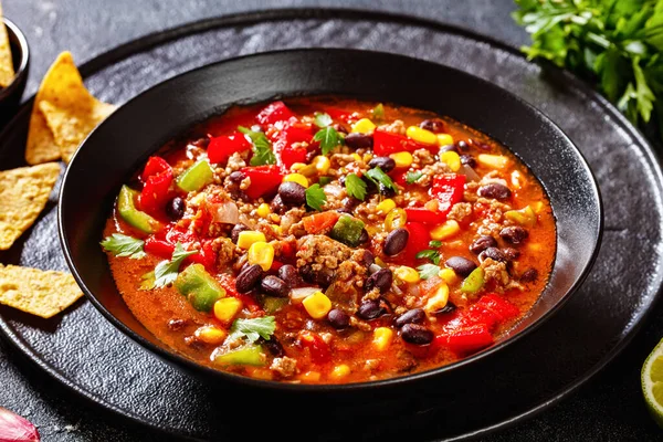 Stock image taco soup of ground beef, tomatoes, chopped green chilis, onions, corn, red beans and taco seasoning in black bowl,  close-up,