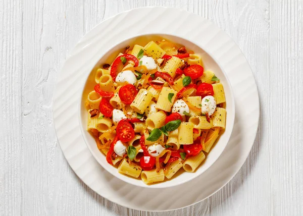 roasted pepper tomato mozzarella pasta salad in white bowl on white wood table, horizontal view from above, flat lay, close-up
