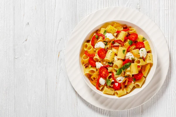 roasted pepper tomato mozzarella pasta salad in white bowl on white wood table, horizontal view from above, flat lay, free space