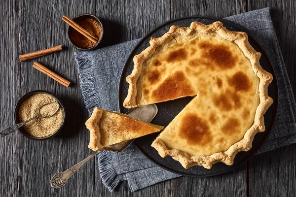 classic sugar cream pie, hoosier pie, indiana custard cream pie on black plate on dark wood table,with cinnamon and brown sugar, landscape view from above, flat lay
