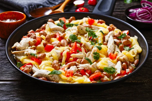 one pan dinner of shredded chicken breast, pinto beans, tomato and mozzarella on dark wood table, close-up