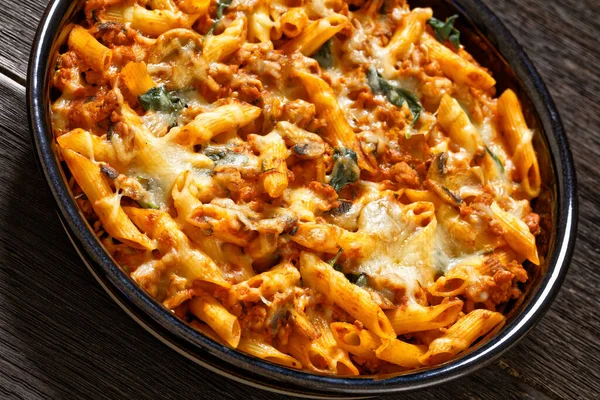 Ground Chicken Pasta Bake with onion, mushrooms, spinach, tomato sauce and mozzarella cheese in baking dish, close-up