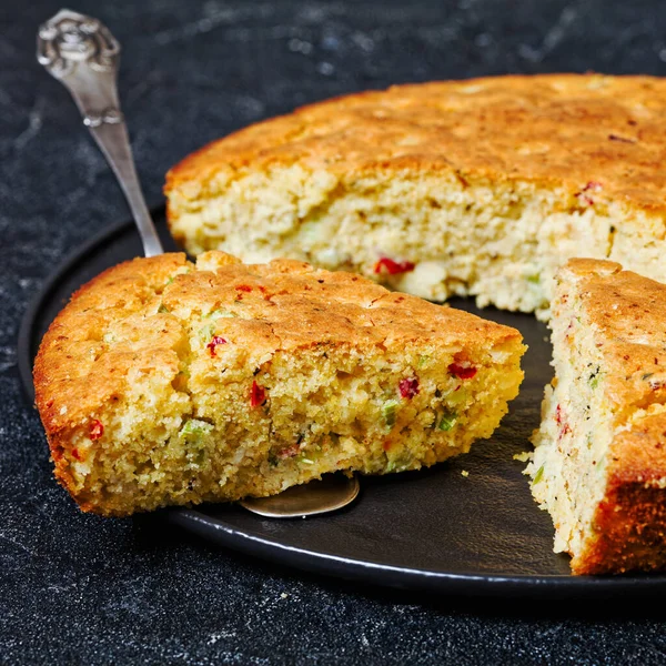 stock image Red pepper Cheddar Celery Cornbread on black plate and a slice on cake shovel on concrete table, horizontal view from above, close-up