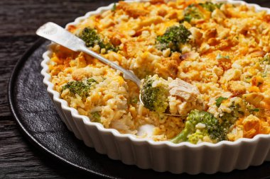 chicken rice broccoli casserole topped with cheddar cheese and crumbled cracker in baking dish on dark wooden table, close-up clipart