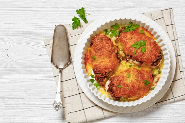 baked chicken breasts topped with caramelized onion and mozzarella cheese in baking dish on white wooden table with cake shovel, horizontal view from above, flat lay, free space
