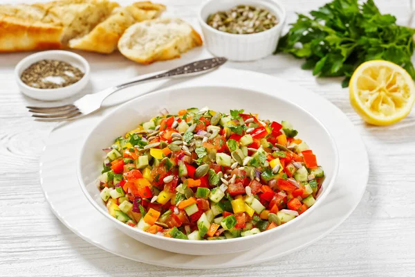 Israeli salad of finely diced tomato, onion, cucumber, and bell peppers, salat katzutz, salat aravi, salat yerakot in white bowl on white wooden table