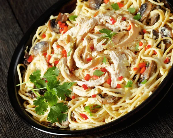 Chicken Pasta Bake with mushrooms, cheese, cream and hot red pepper in  baking dish on dark wooden table, dutch angle view, close-up