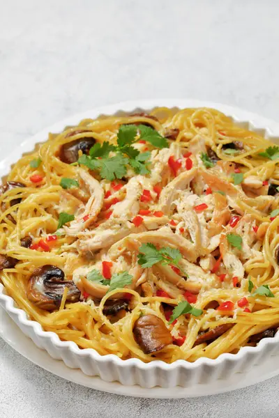 Chicken Spaghetti Bake with mushrooms, cheese, cream and hot red pepper in white baking dish on concrete table, vertical view from above, close-up, free space