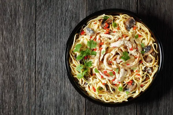Chicken Spaghetti casserole with mushrooms, cheese, cream and hot red pepper in  baking dish on dark wooden table, horizontal view from above, flat lay, free space