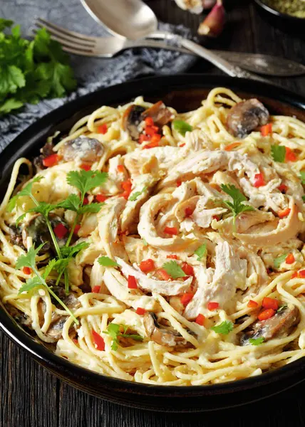 Chicken Pasta Bake with mushrooms, cheese, cream and hot red pepper in  baking dish on dark wooden table with ingredients, vertical view from above, close-up