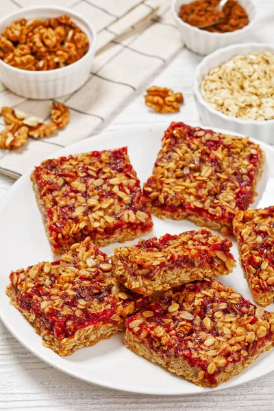Red berry Shortbread Bars with Rolled Oat and Nut Topping on white plate on white wooden table, vertical view from above, close-up