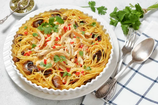 Chicken Spaghetti Bake with mushrooms, cheese, cream and hot red pepper in white baking dish on concrete table, horizontal view from above