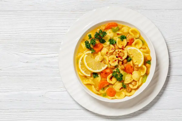 orecchiette veggies chickpea soup in white bowl on white wooden table, horizontal view from above, flat lay, free space