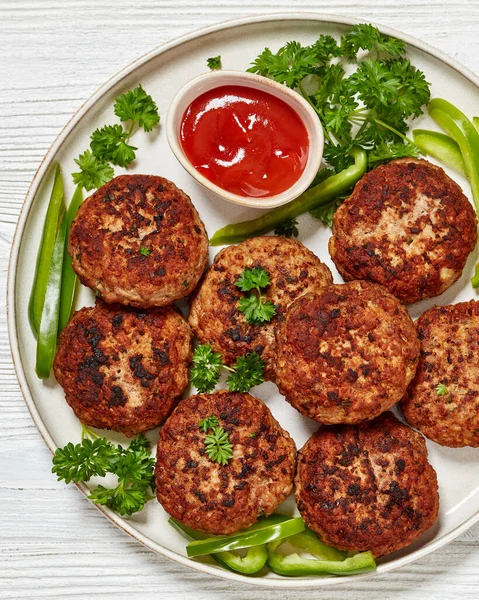 german frikadellen of ground beef and pork, breadcrumbs, onions and spices on plate with tomato sauce on white wooden table, horizontal view from above, flat lay, close-up
