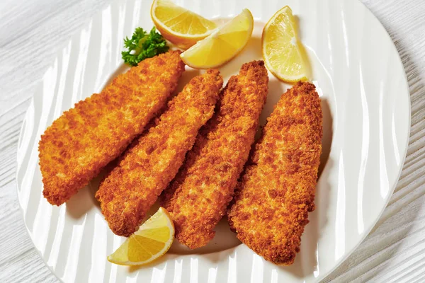 breaded fish fillet baked in oven served with yellow mustard on white plate on white wooden table, close-up