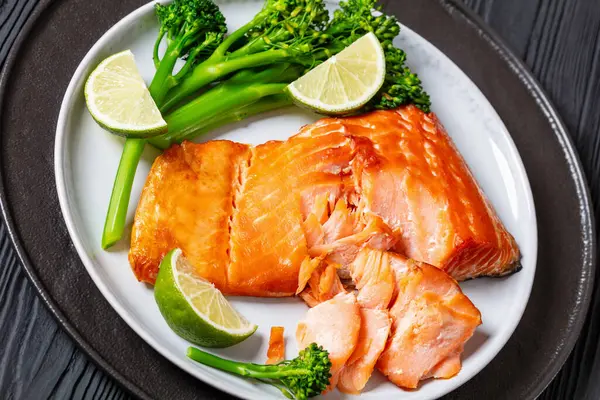hot smoked salmon with cooked broccoli and lime on plate on black wooden table, close-up
