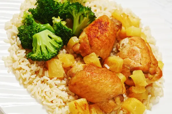 roasted boneless chicken thighs with pineapple chunks, brown rice and broccoli on white plate, close-up