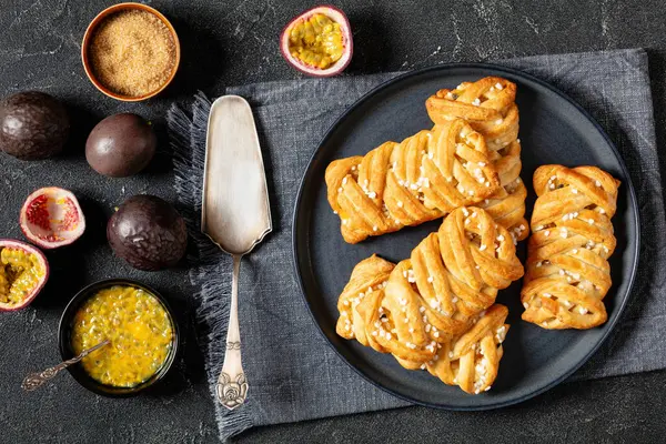 stock image passion fruit puff pastry turnovers on plate on concrete table with cake shovel and ingredients, horizontal view from above, flat lay