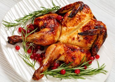 butterflied or spatchcock roast whole chicken on white plate with rosemary and cranberry on wooden table, close-up clipart