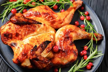 butterflied or spatchcock roast whole chicken on dark grey plate with rosemary and cranberry on black wooden table, close-up clipart