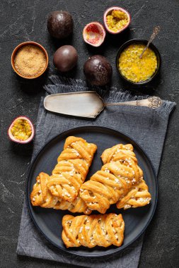 passion fruit turnovers on plate on concrete table with cake shovel and ingredients, vertical view from above clipart