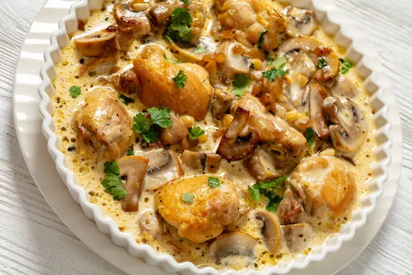 chicken thighs in a creamy mushroom garlic sauce with herbs and parmesan cheese in white baking dish on white wooden table, close-up