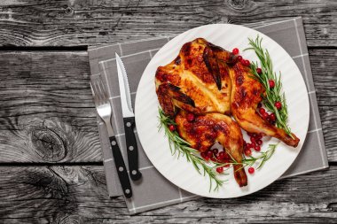 butterflied roast whole chicken on plate with rosemary and cranberry, on grey wooden rustic table with cutlery, horizontal view from above, flat lay, free space clipart