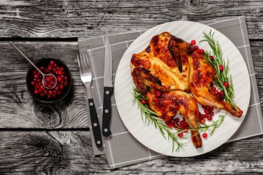 butterflied or spatchcock roast whole chicken on plate with rosemary and cranberry, on grey wooden rustic table with cutlery, horizontal view from above, flat lay clipart
