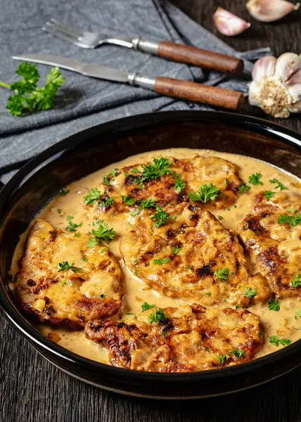 stock image creamy smothered pork chops cooked in onion gravy in baking dish on dark oak wooden table, vertical view from above, close-up