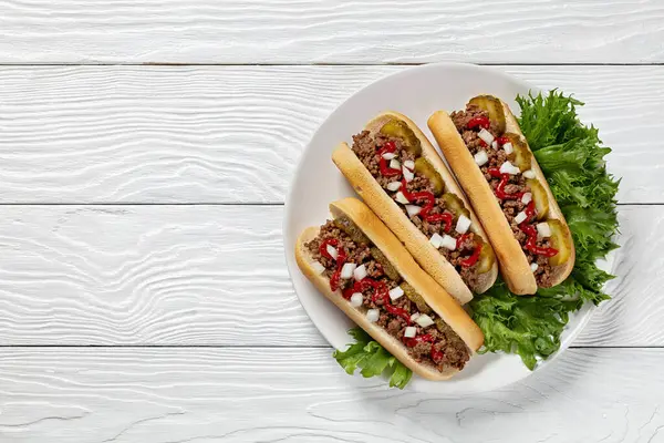 stock image Midwestern Loose Meat Sandwiches, Juicy burgers of ground beef topped with pickles, raw onion and ketchup on white plate on white wooden table, horizontal view from above, flat lay, copy space