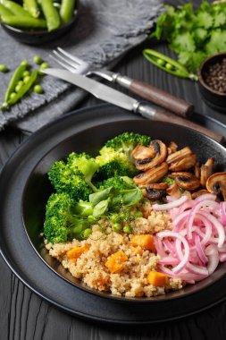 quinoa with sweet potato, sauteed mushrooms, pickled red onion, green peas, boiled broccoli in black bowl on black wood table with cutlery, cilantro, fresh pea pods, vertical view, close-up clipart