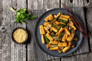 Japanese Hibachi Zucchini stir-fried with onion in soy sauce and teriyaki sauce sprinkled with sesame seeds and red pepper flakes on plate on rustic wooden table with chopsticks, flat lay clipart